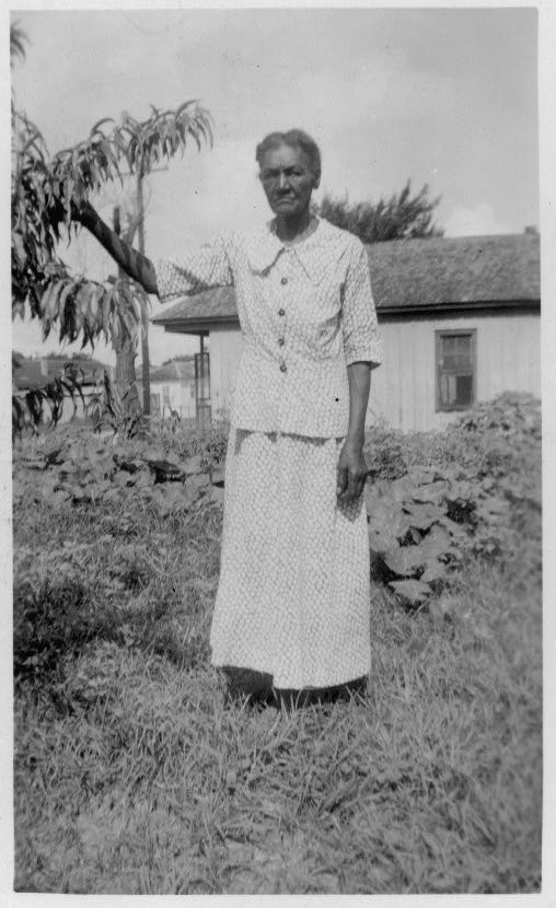 Portrait of Sarah Ford standing in front of a house with her right hand holding a tree branch.